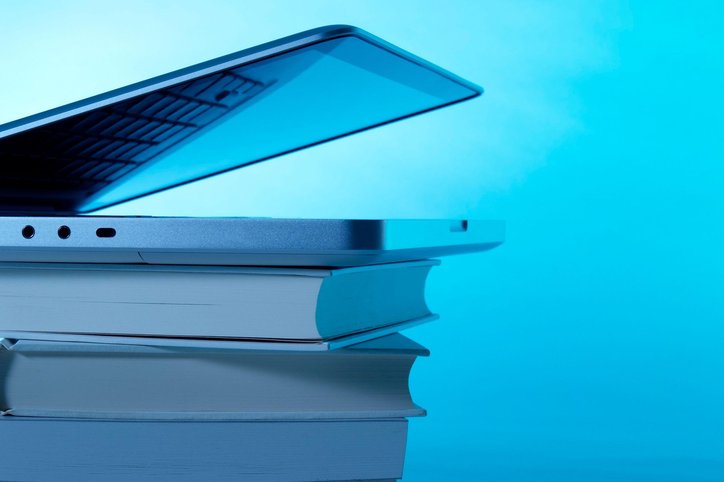 A half-opened laptop lies on a pile of books