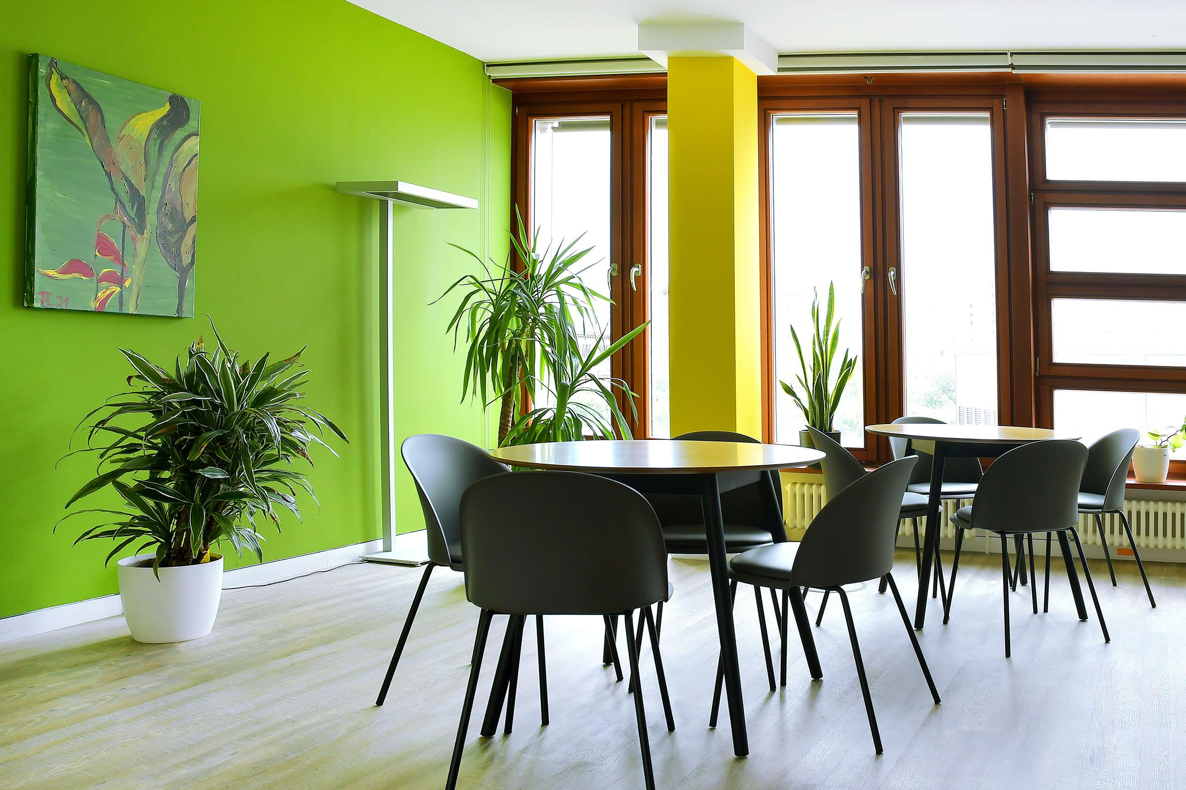 Tischgruppen in einem Raum mit grüner Wand und Pflanzen