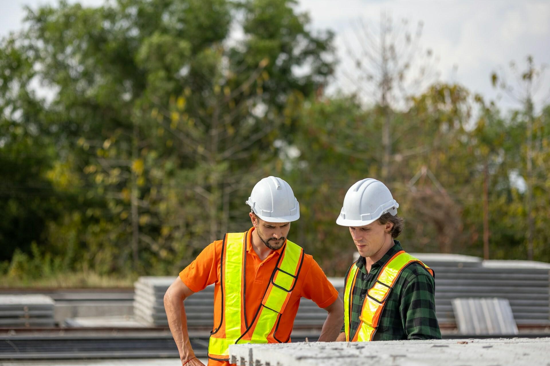 Baustelle Two men wearing helmets and safety vests are standing on a construction site, inspecting something