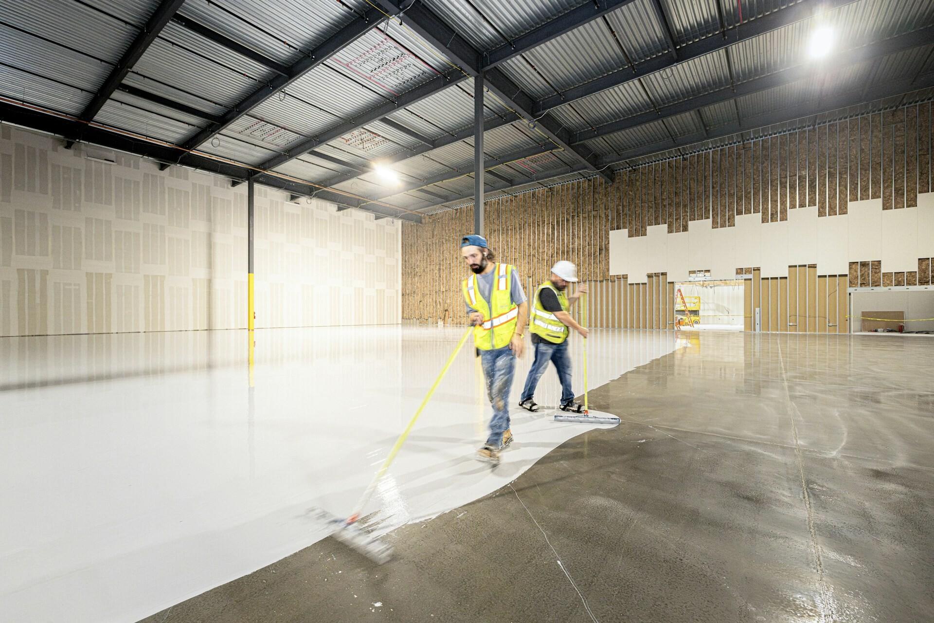 Boden streichen Two workers wearing safety vests are painting the floor of a warehouse white