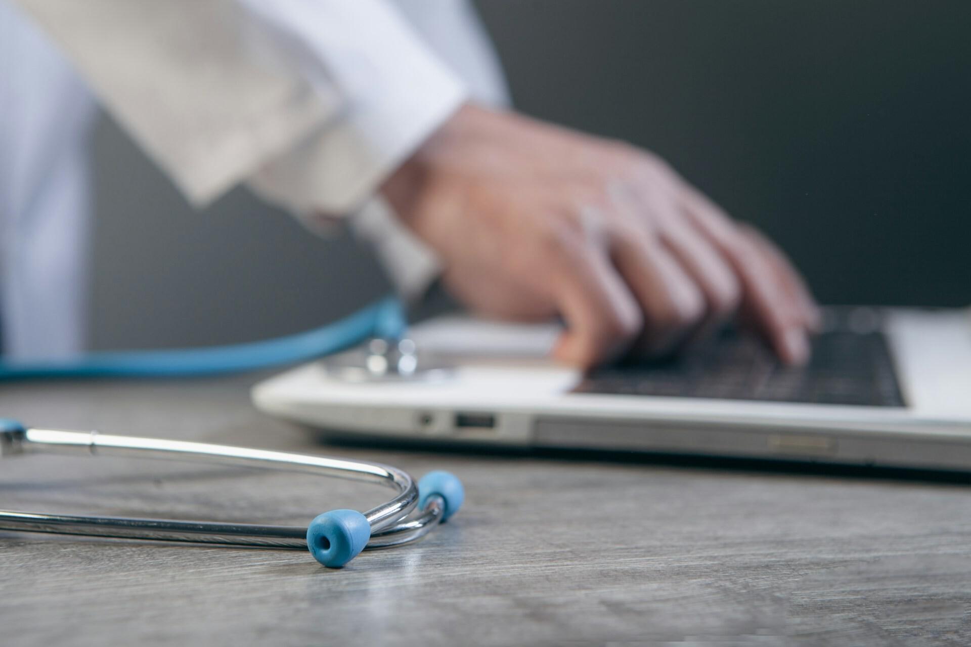 Arzt tippt auf Laptop A person's hands are typing on a laptop; a stethoscope lies in front of it