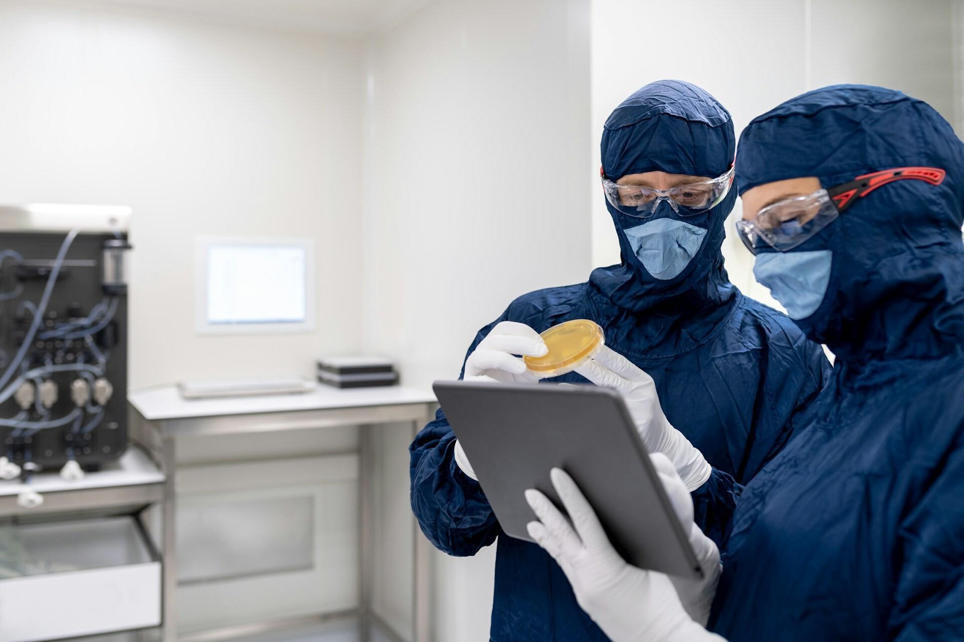Labor Two people in protective suits are examining a sample together by looking at a tablet