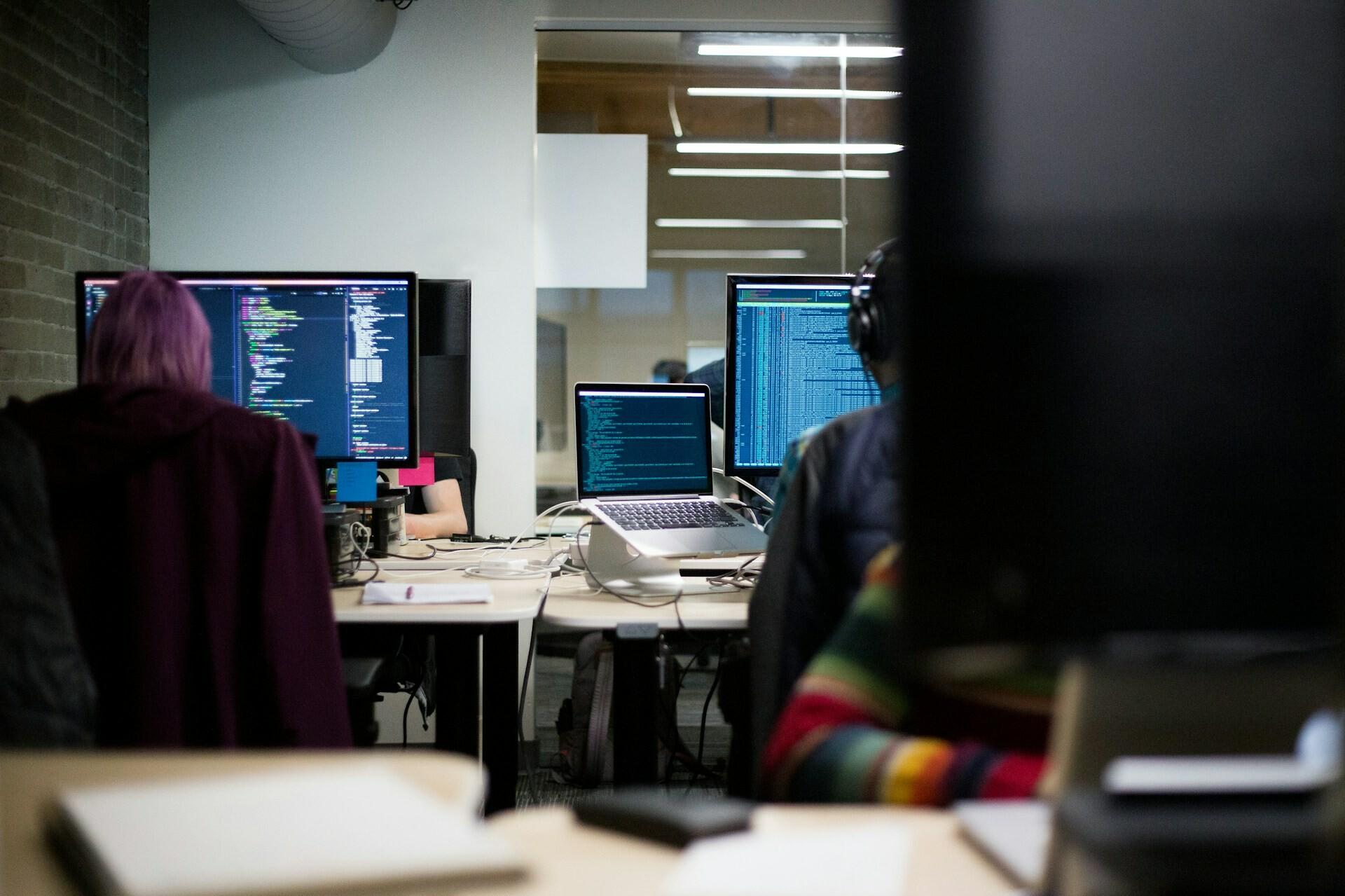 Software-Entwicklung Mehrere Personen in einem Büro arbeiten vor ihren Bildschirmen an Code-Projekten