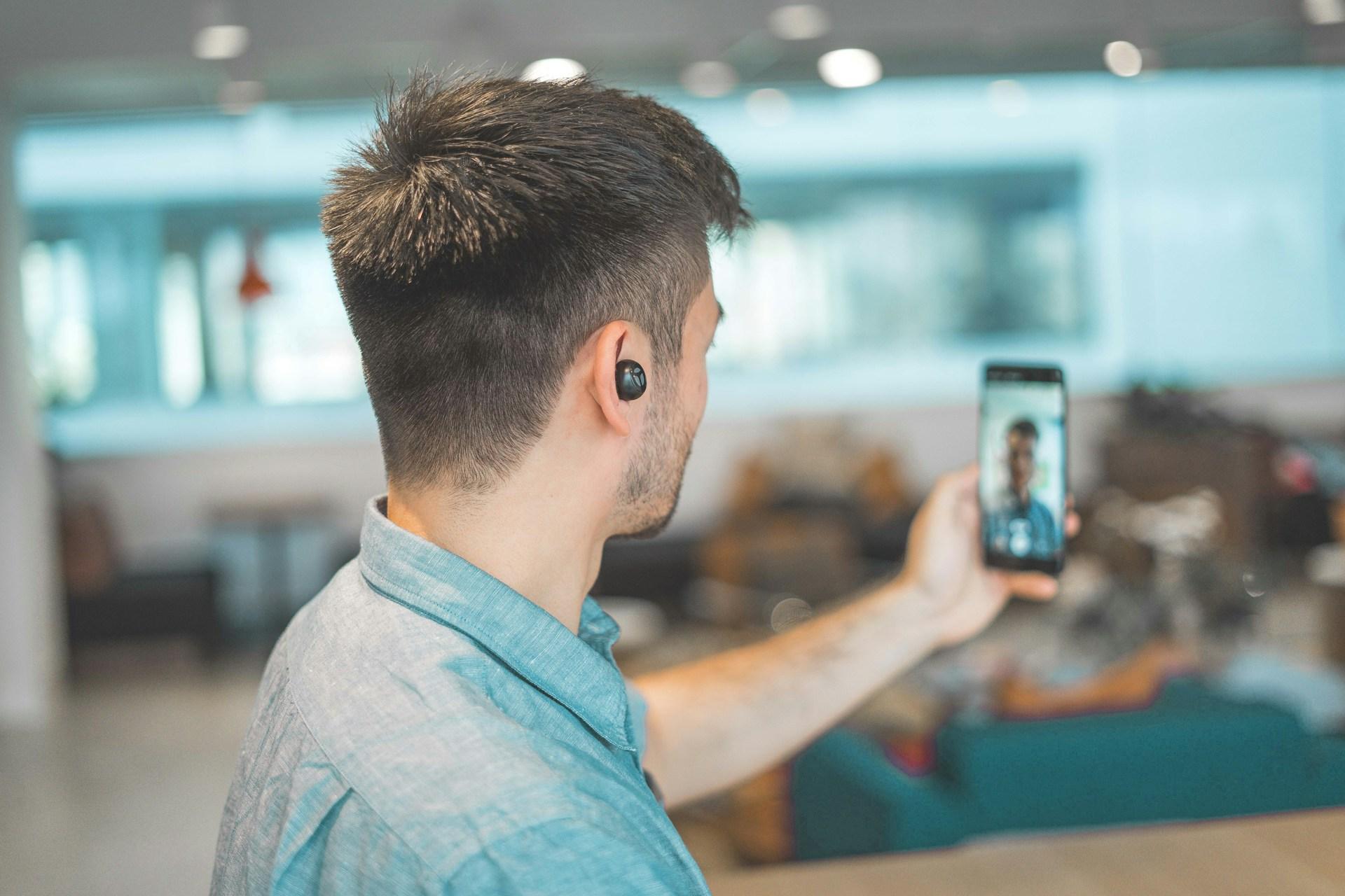 Video-Call A man with an earbud is on a video call on his cell phone