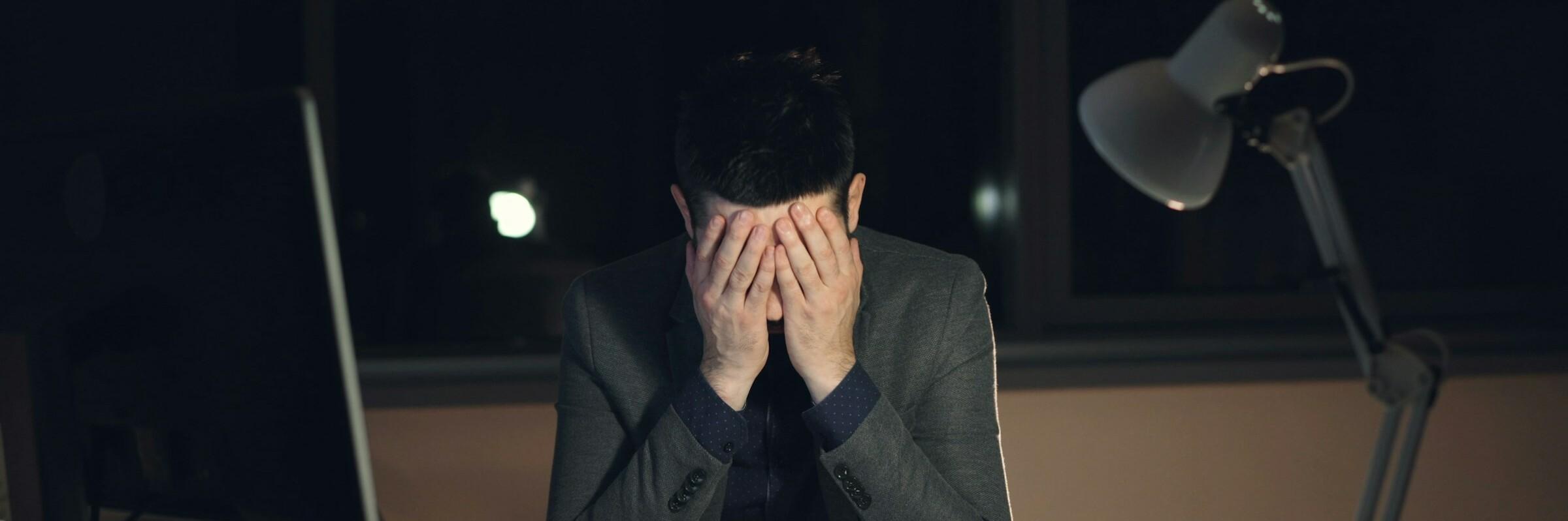 Ein Mann sitzt am Schreibtisch und hat seinen Kopf in den Händen vergraben.