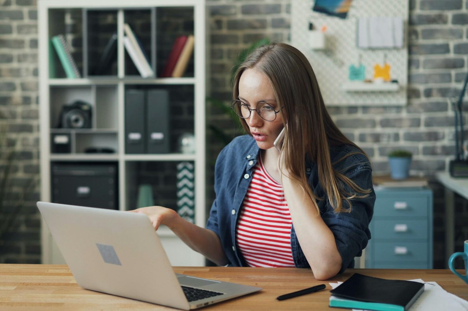 Telefonat A woman is talking on her cell phone at her desk while looking at her laptop at the same time