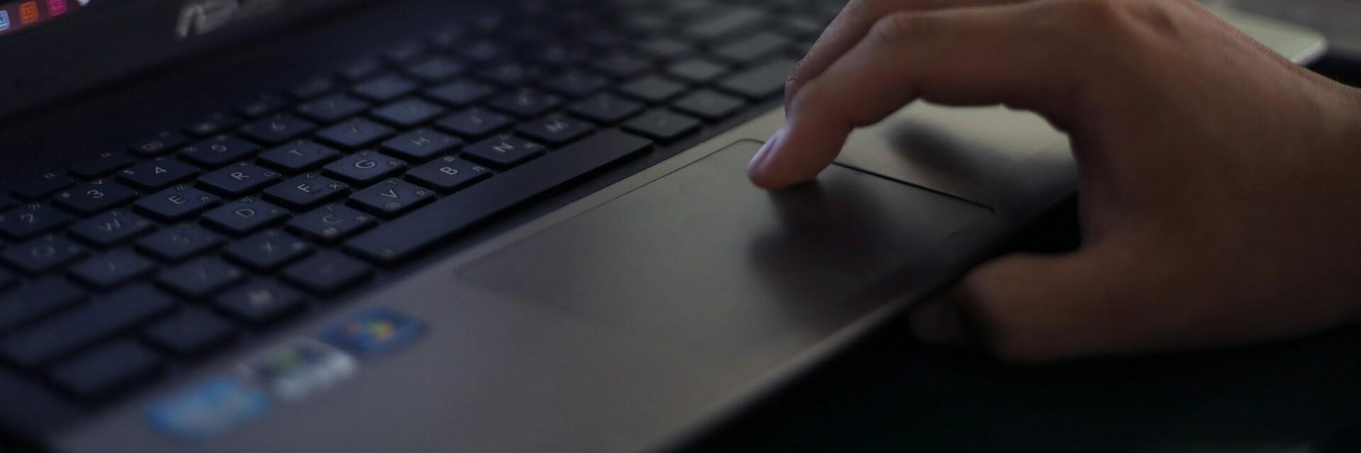 Hand auf Laptop Eine Person bedient das Mousepad ihres Laptops