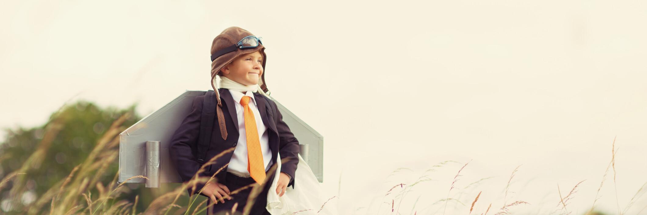 Boy wearing a helmet and cape in a superhero pose