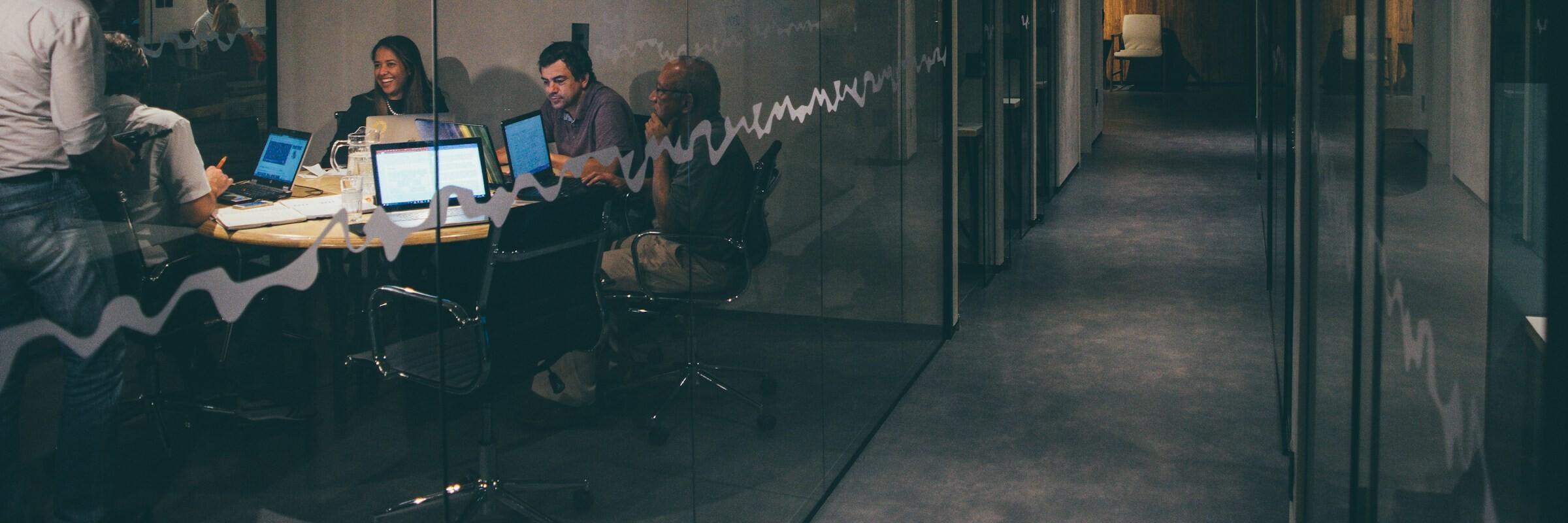 Arbeit im Büro Mehrere Personen sitzen im Büro um einen Tisch herum an ihren Laptops und arbeiten