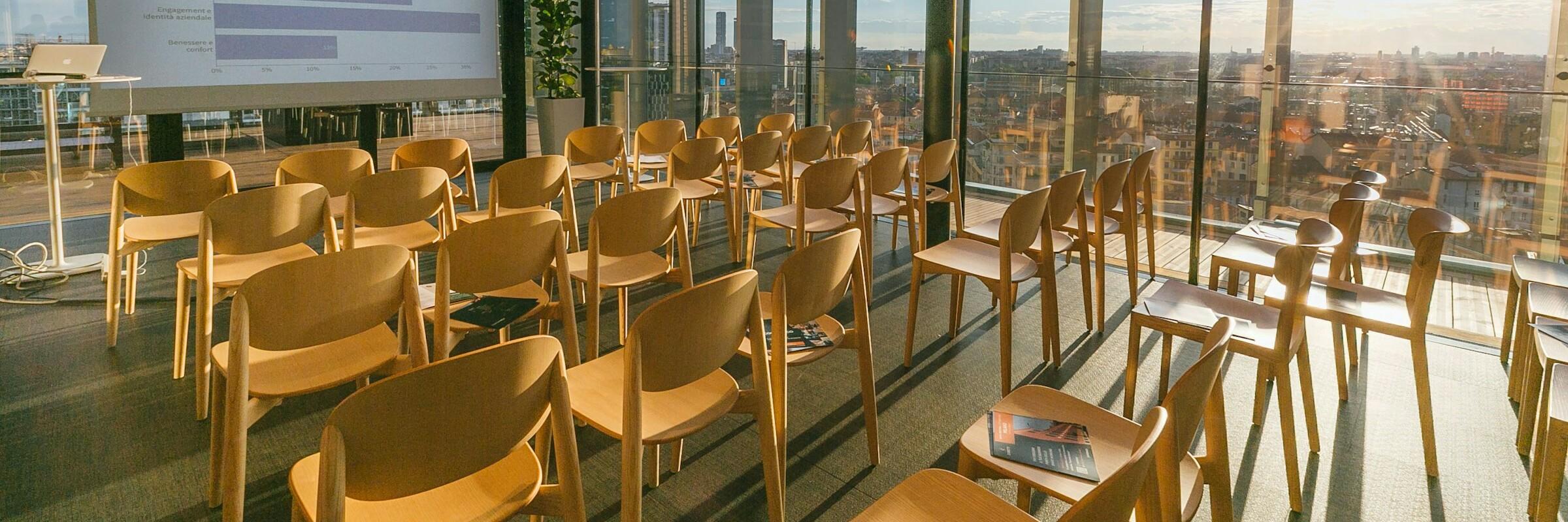 Holzstühle in einem Konferenzraum In einem verglasten Konferenzraum stehen Holzstühle, vorne ist eine Präsentation aufgebaut